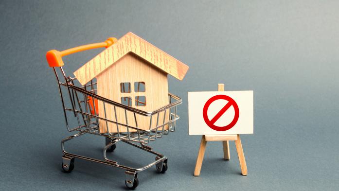Wood replica of a house inside a shopping cart with a "no" symbol beside it on an easel