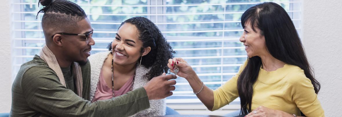 Young couple meeting with Real Estate Agent, handing over key - stock photo  A young African-American couple meeting with a real estate agent, a mature mixed race Chinese and Caucasian woman, sitting at a table by a window. They are smiling at each other and the Real Estate Agent is handing over the key to their new home or rental.