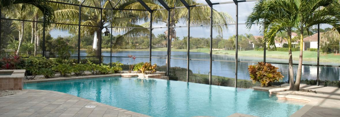 A backyard pool located in a tropical setting covered by a screen lanai. Lake in behind.